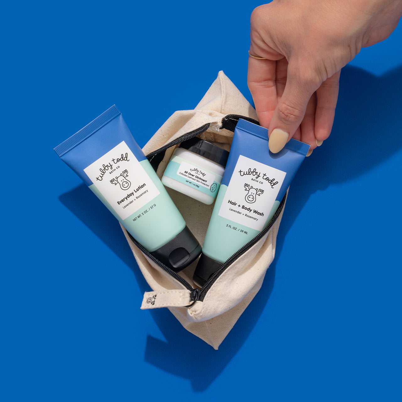 A hand grabbing the Lavender Rosemary 2oz Hair + Body Wash tube from the Try Tubby Kit's the canvas travel bag.
